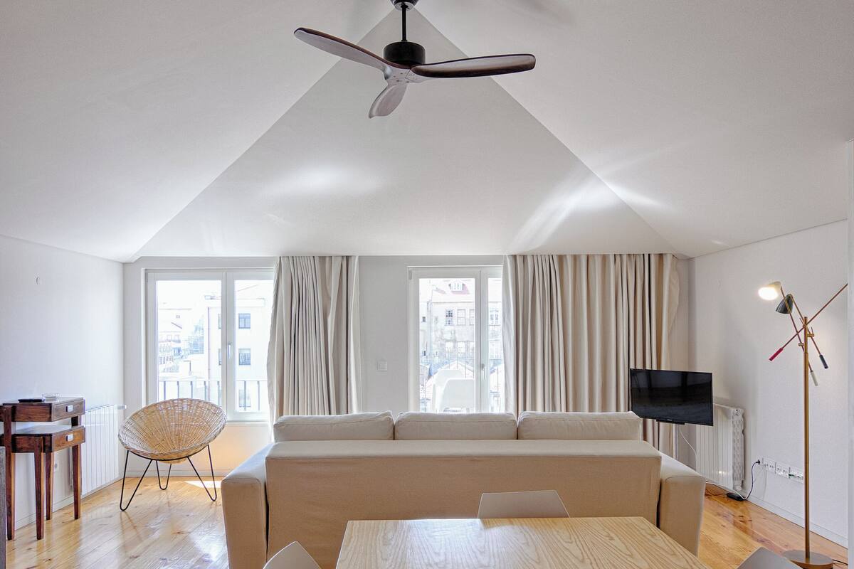 A spacious living area with a wooden dining table, a sofa, and a ceiling fan.