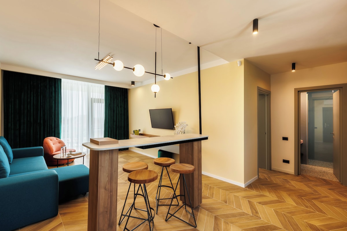 Una sala moderna con un sofá, una mesa de centro y un televisor. Cuenta con una zona de bar con taburetes y una barra. El piso presenta un diseño tipo espiga.