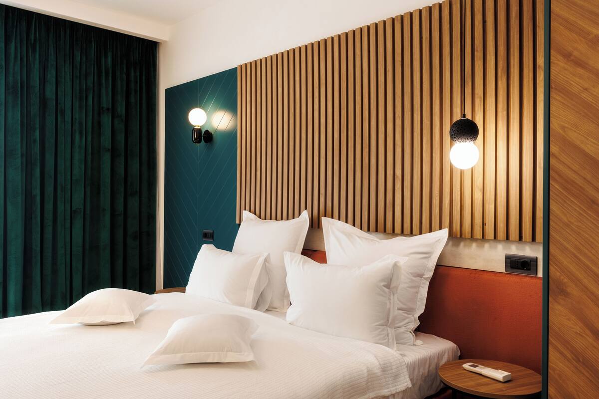 Una habitación de hotel moderna con cama, almohadas, una mesita de noche y una lámpara de pared.