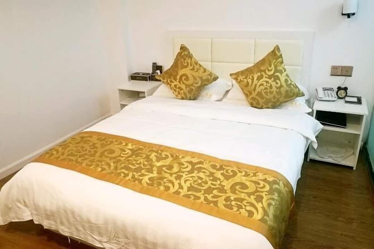 Una habitación de hotel con una cama, dos mesitas de noche y un teléfono fijo en la pared.