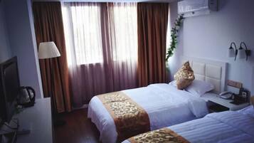 A hotel room with two beds, a desk with a lamp, and a TV.