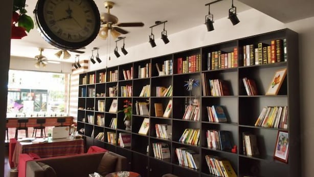 Una biblioteca con una estantería grande llena de libros, un ventilador de techo y un reloj.