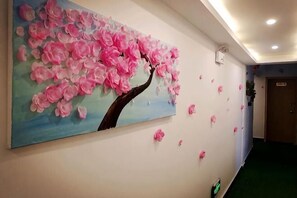 Un couloir ornĂ© dâun grand tableau reprĂ©sentant des fleurs roses, avec une porte et un tapis vert.