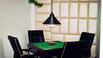 A room with a billiards table, four black chairs, and a hanging pendant light.