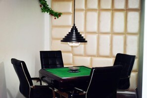 Una habitación con mesa de billar, cuatro sillas negras y una lámpara colgante.