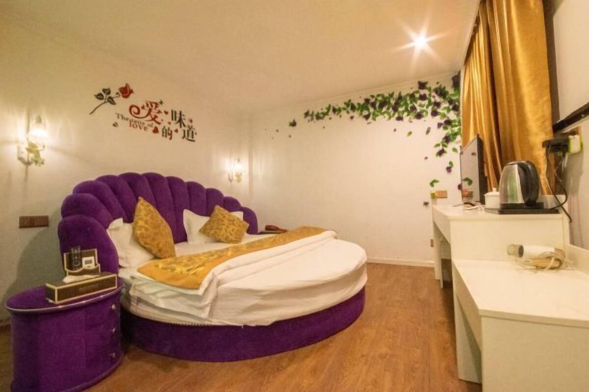 Un dormitorio con una cama redonda, una mesita de noche pequeña, un escritorio y una pared con detalles decorativos.
