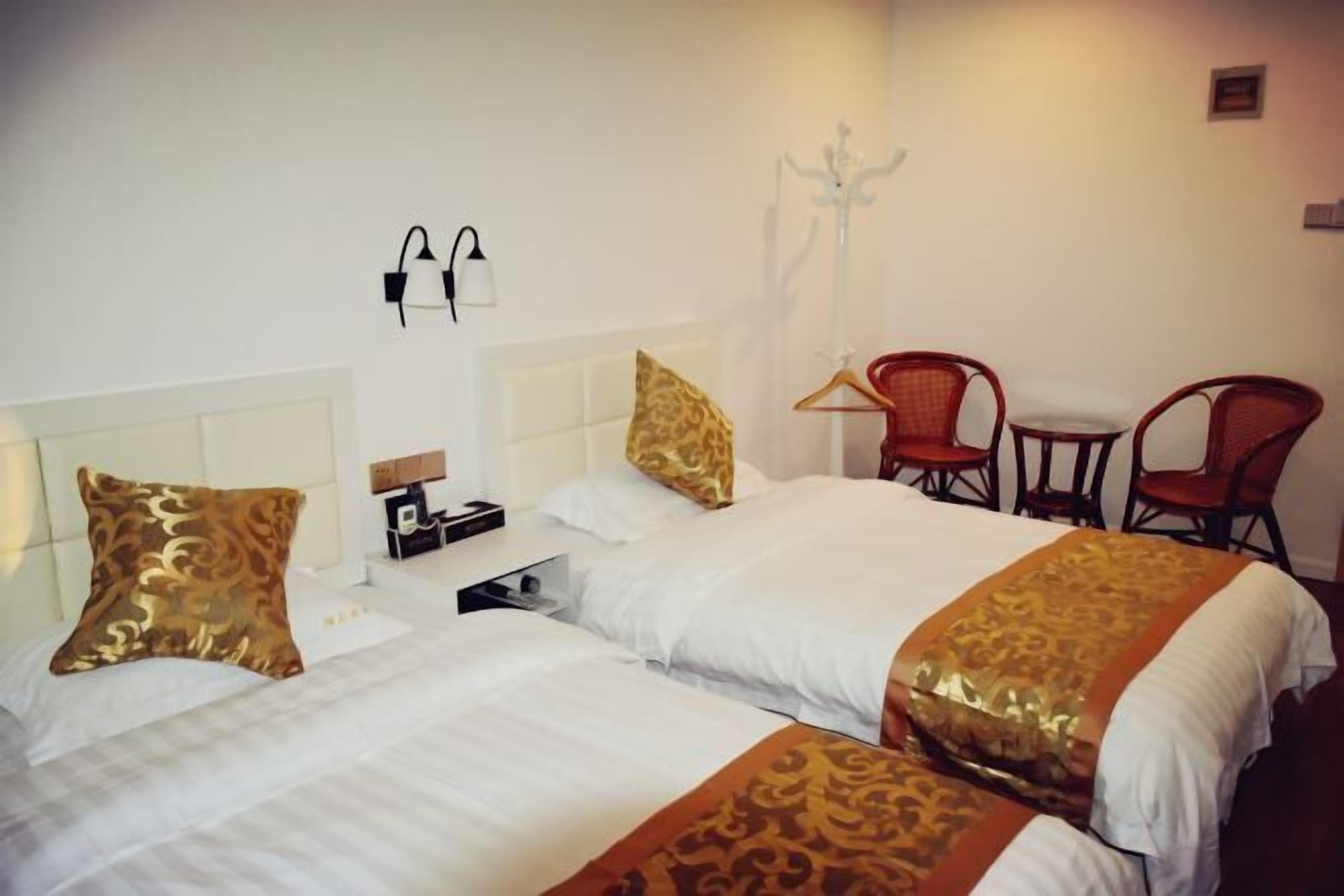 A hotel room with two beds, a nightstand, a lamp, and a coat rack with hangers.