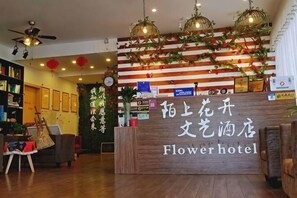 A hotel reception desk with a wooden counter, a sign reading 'Flowerhotel,' and a wall decorated with red lanterns and greenery. - Moshang Huakai Liyi Hotel (Wuhu Limin Middle Road Branch) (Wuhu)