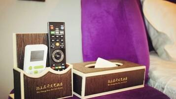 A hotel room with a bed, a purple headboard, a remote control, and a tissue box.