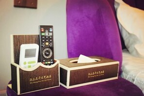 Une chambre d’hôtel avec un lit, une tête de lit violette, une télécommande et une boîte de mouchoirs.