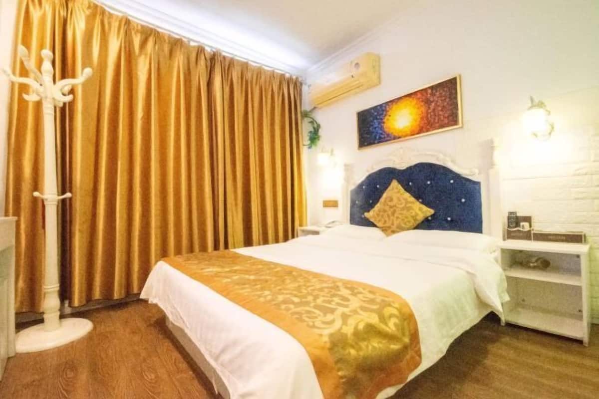 Una habitación de hotel con una cama grande, cabecera con almohada decorativa, mesita de noche con lámpara y un cuadro en la pared.