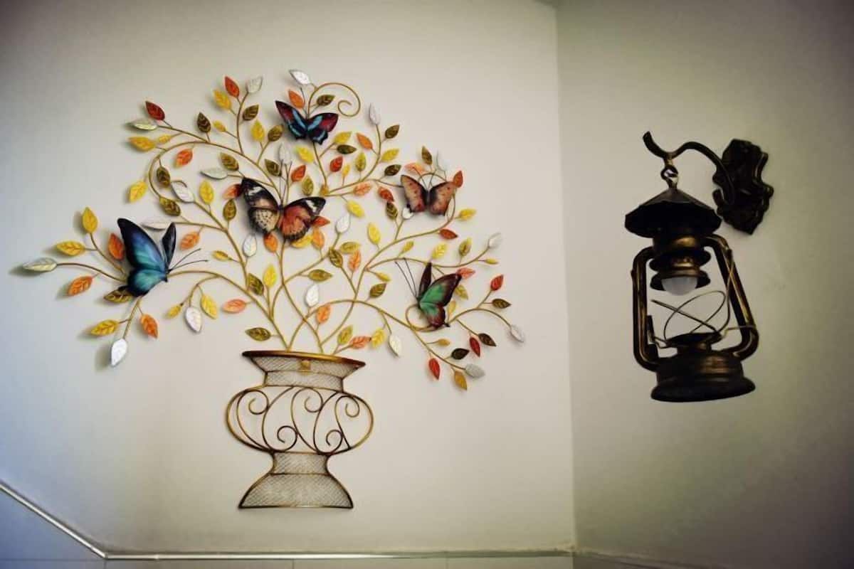 Una pared con un detalle decorativo de metal representando un jarrón con hojas y mariposas, y un farol.