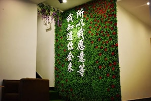 Un mur orné de feuillage vert et de fleurs rouges, ainsi que de caractères chinois.