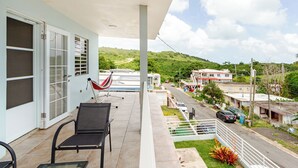 A balcony with a hammock, a chair, and a view of a road and buildings in the distance. - 5 minutes from Seven Seas Beach Quiet Escape in Fajardo with Ocean View (Fajardo)