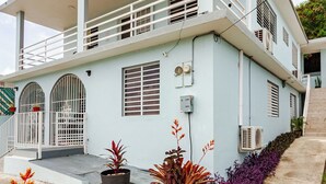 A light blue two-story house with a balcony, a front door, and a small garden with plants. - 5 minutes from Seven Seas Beach Quiet Escape in Fajardo with Ocean View (Fajardo)