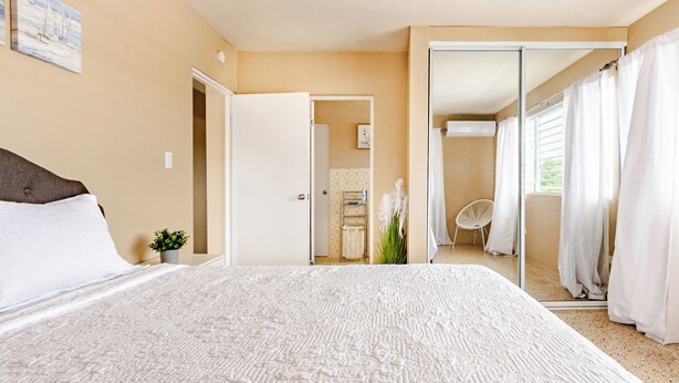 A bedroom with a large bed, a door leading to a bathroom, and a view of the bathroom through a mirror. - 5 minutes from Seven Seas Beach Quiet Escape in Fajardo with Ocean View (Fajardo)