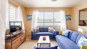 A living room with a sofa, a coffee table, a TV on a wooden cabinet, and a window with curtains. - 5 minutes from Seven Seas Beach Quiet Escape in Fajardo with Ocean View (Fajardo)