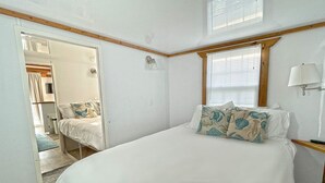 Une chambre à coucher avec un grand lit, une fenêtre avec des stores, une lampe de chevet et une porte donnant sur une salle de bain.