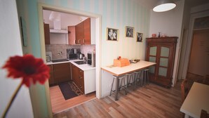 Une cuisine compacte avec des meubles en bois, un plan de travail blanc et un tabouret de bar. Des tableaux encadrés ornent le mur, et on y trouve également un meuble en bois doté de portes en verre.
