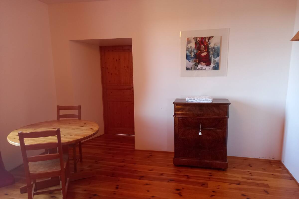 Een kamer met een houten eettafel, stoelen, een kast en een schilderij aan de muur.