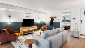 A modern living room with a grey sofa, orange armchair, wooden sideboard, and a flat-screen TV. - Sosuite | 2BR Apt w Laundry, Private Entrance (Philadelphia)