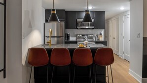 A modern kitchen with black cabinets, stainless steel appliances, and a central island with four red chairs. - Sosuite | 2BR Apt w Laundry, Private Entrance (Philadelphia)