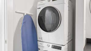 A laundry room with stacked washers and dryers, a hanging blue garment, and a white door.