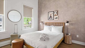 A neatly arranged bedroom with a wooden bed, a round mirror, and a small bedside table with a lamp.