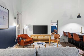 Ein modernes Wohnzimmer mit großem Flachbildfernseher, einer Couch, einem Couchtisch und einem Essbereich mit Stühlen.
