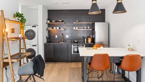 Una cocina moderna con armarios oscuros, encimera blanca y una zona de comedor con sillas naranjas.