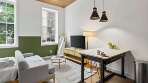 A modern living room with a sofa, a small table, a TV, and a lamp. - Sosuite | Studio Apt w Laundry, Courtyard View (Philadelphia)