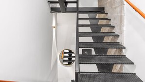 A staircase with black steps and metal railings, white walls, and a brick wall. - Sosuite | Studio Apt w Laundry, Courtyard View (Philadelphia)