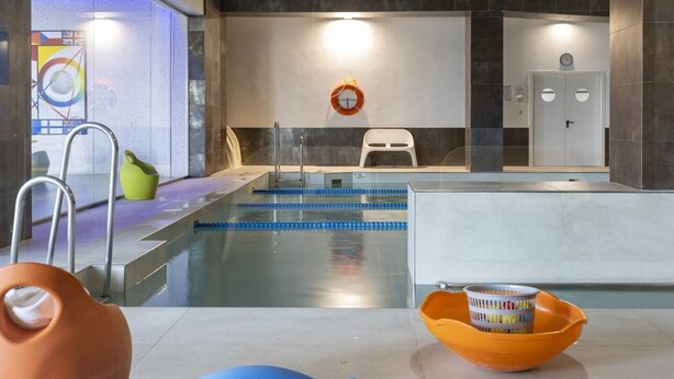 Una piscina interior con carriles delimitados, un flotador salvavidas y un reloj en la pared.