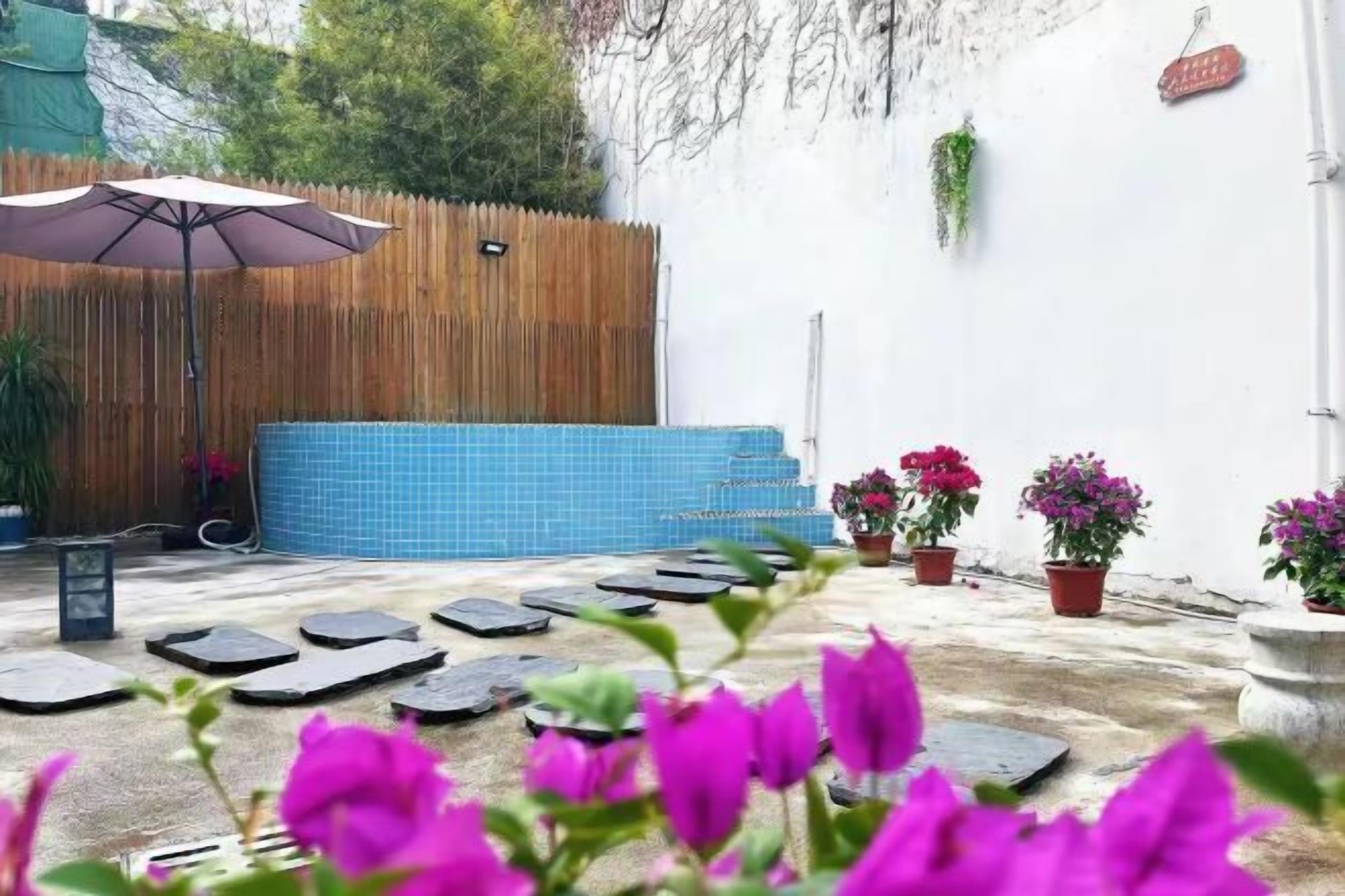 Een terras met een blauw betegeld zwembad, stapelstenen, plantenbakken en een houten omheining.