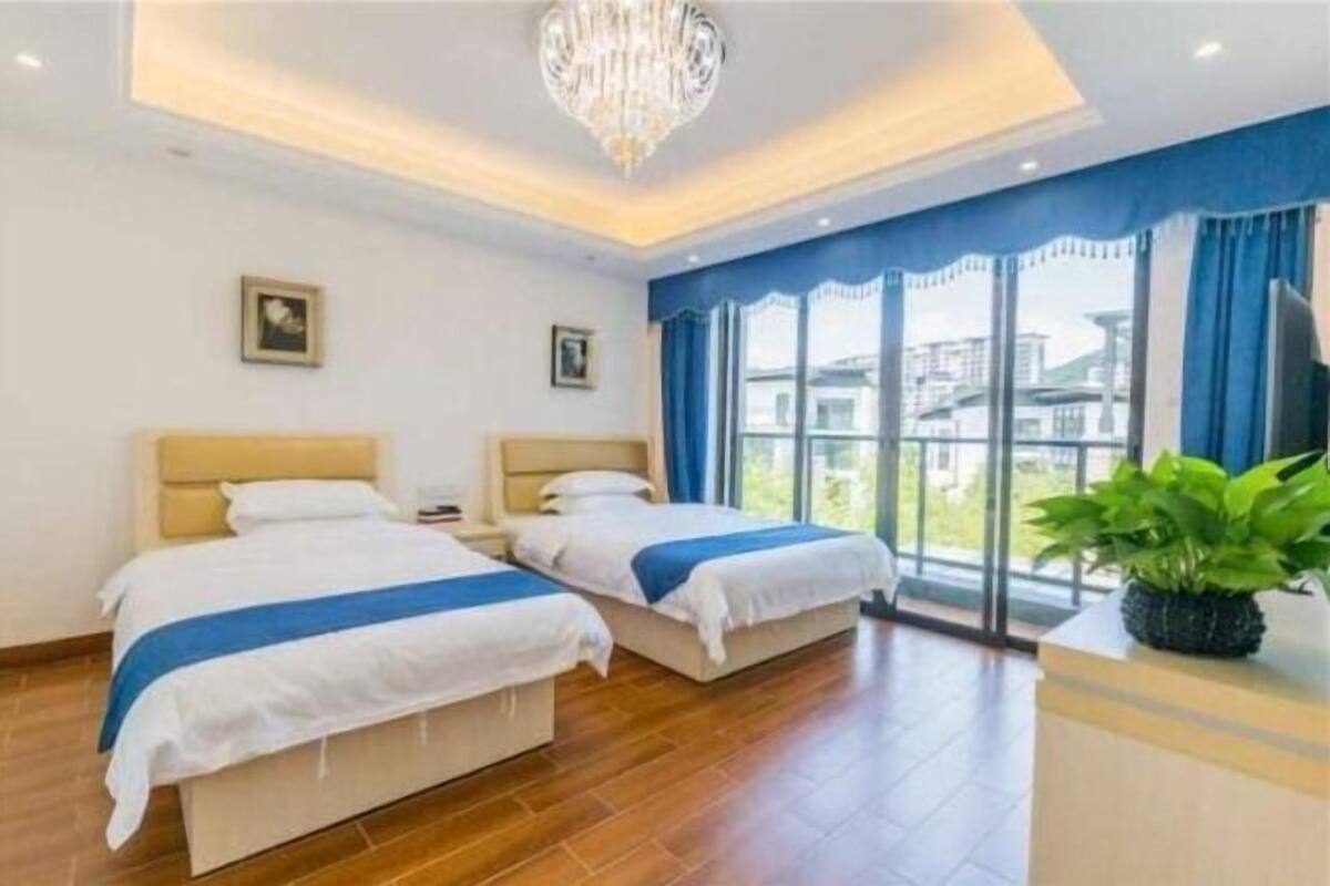Une chambre d’hôtel avec deux lits, un lustre et de grandes fenêtres ornées de rideaux bleus.