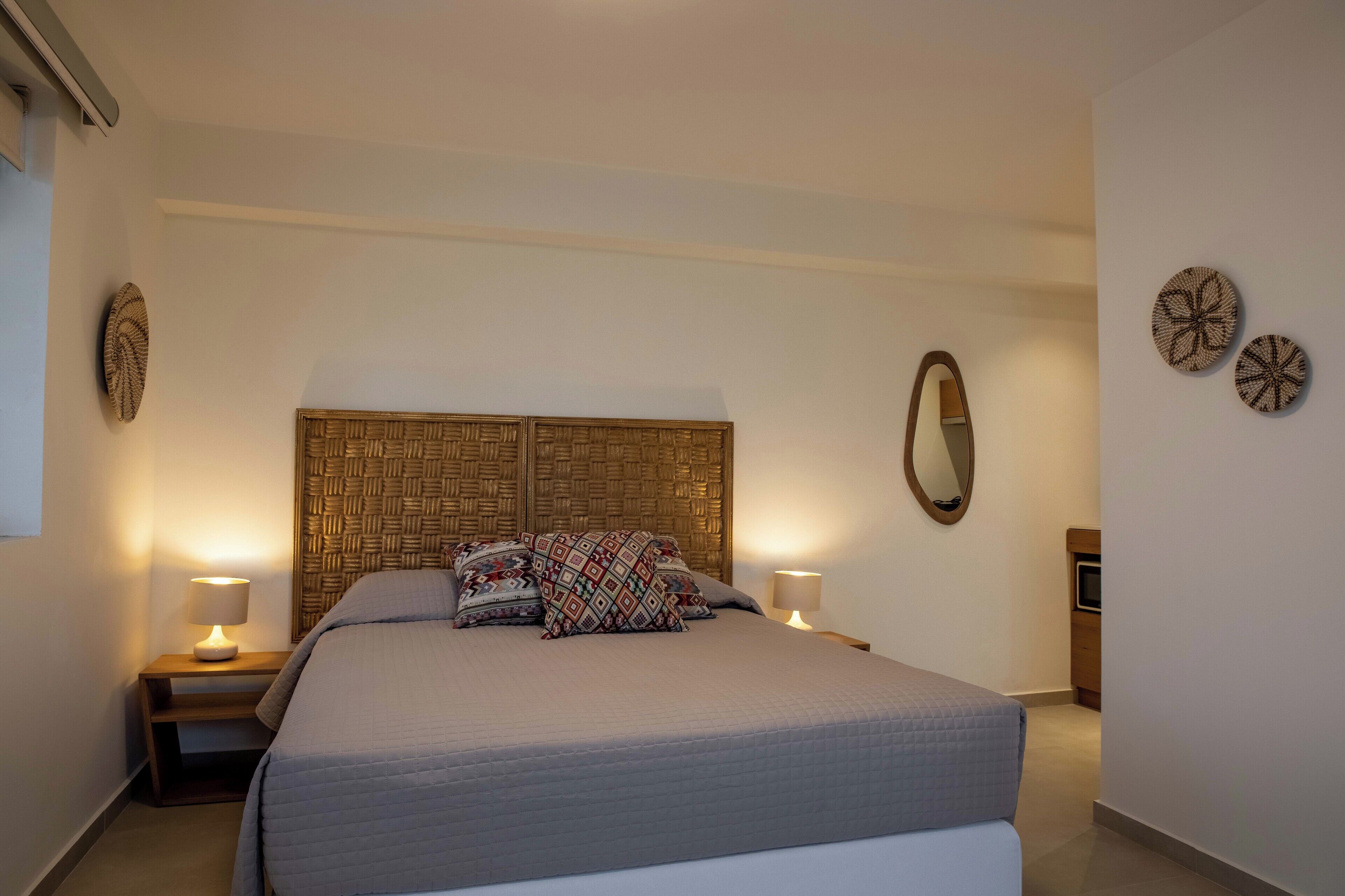 A neatly made bed with patterned pillows, a bedside lamp, and a woven headboard.
