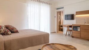 Habitación de hotel moderna con cama, mesita de madera, escritorio con silla, televisor y microondas.