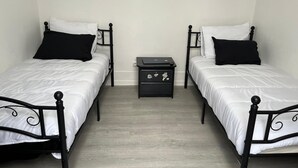 Ein Zimmer mit zwei Einzelbetten, jeweils mit schwarzem Kopfteil und weißer Bettwäsche, und einem kleinen, schwarzen Nachttisch mit Schubladen dazwischen.