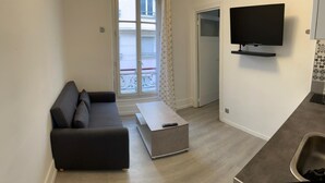 Ein modernes Wohnzimmer mit einer grauen Couch, einem kleinen Couchtisch und einem Wand-Fernseher.