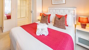 Una cama bien hecha con una colcha roja, dos almohadas y un juego de toallas.