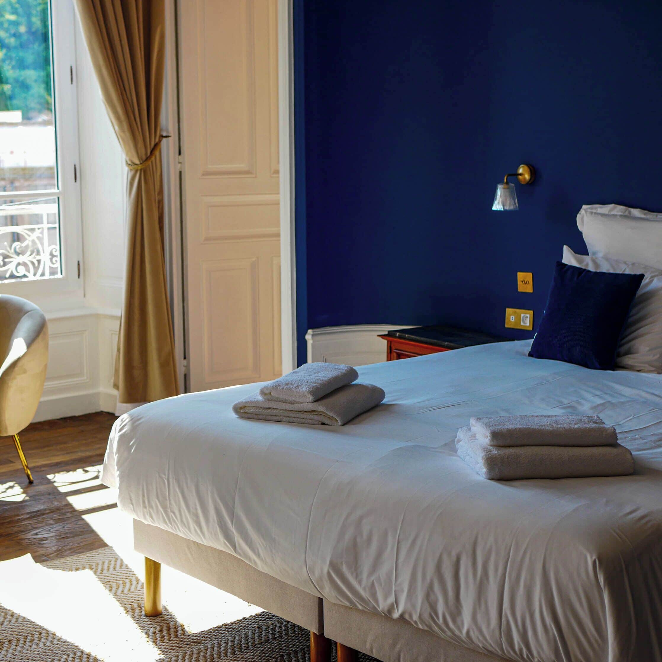 A hotel room with a large bed, a chair, a nightstand, and a window with curtains.
