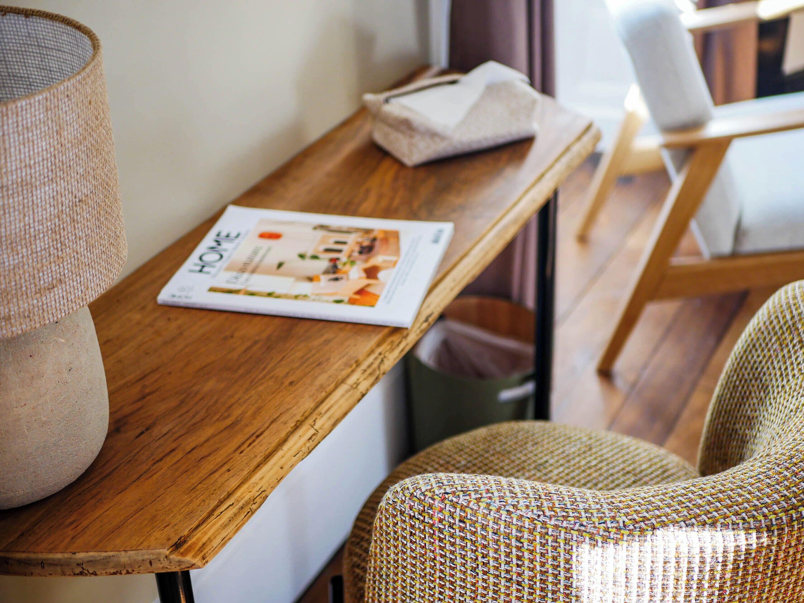 A wooden table with a magazine, a woven lamp, and a chair.