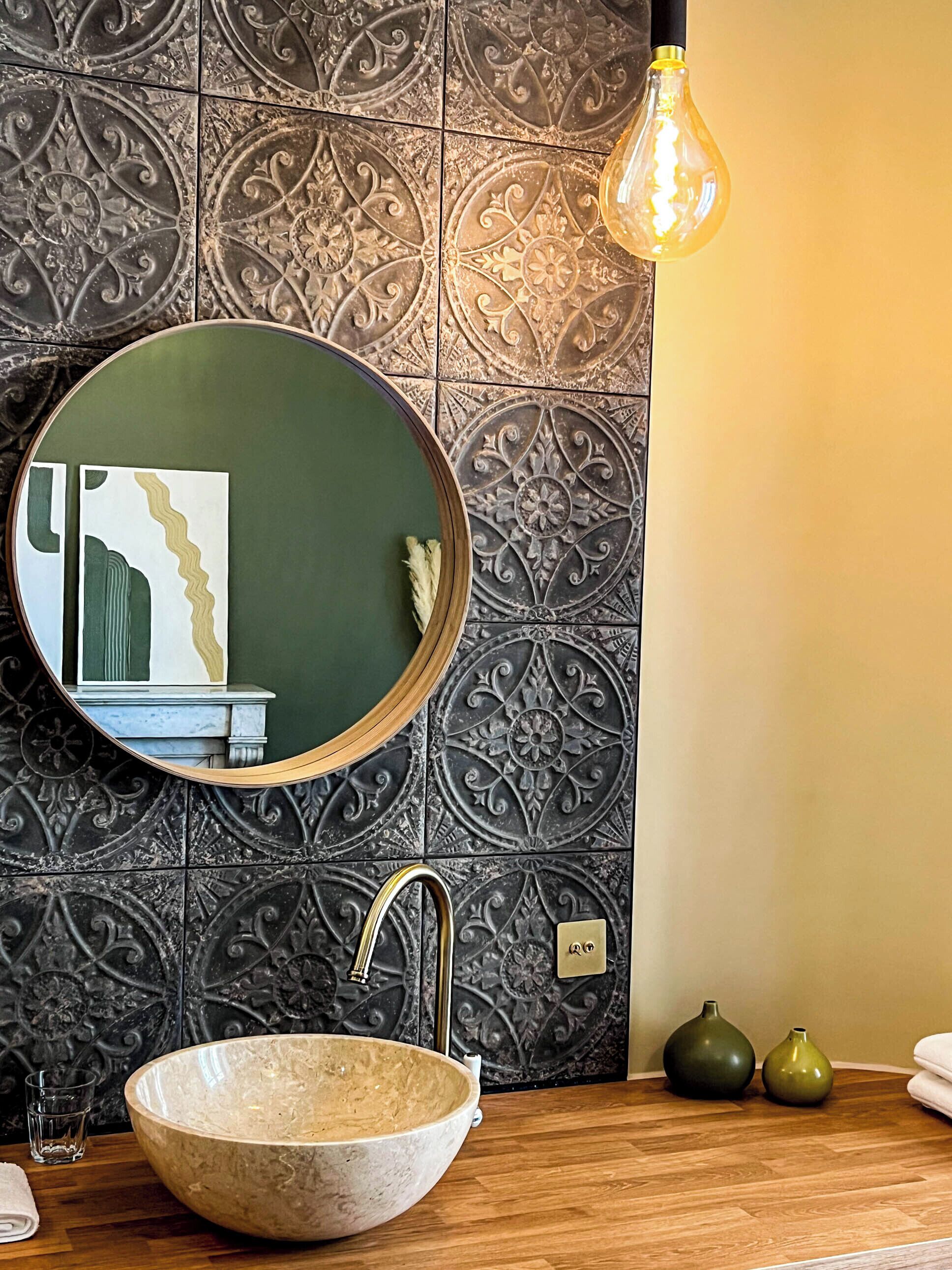 A bathroom with a round mirror, a sink, and decorative tiles.
