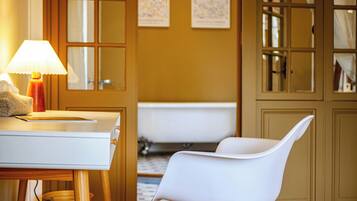 A bathroom with a bathtub, a white chair, a table with a lamp, and a tissue box.
