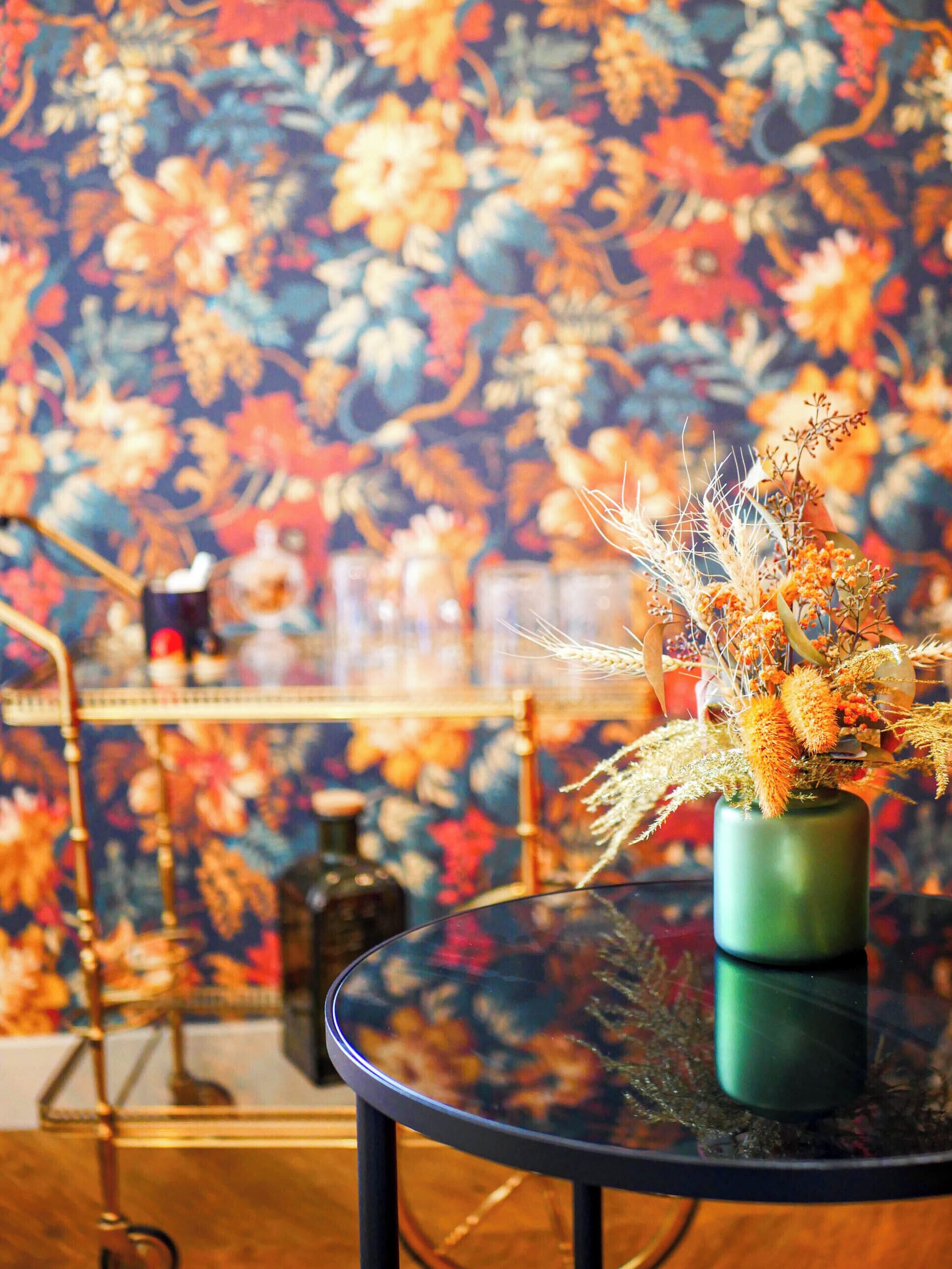 Une table ronde en verre sur laquelle se trouve un vase vert contenant des plantes et des fleurs séchées.