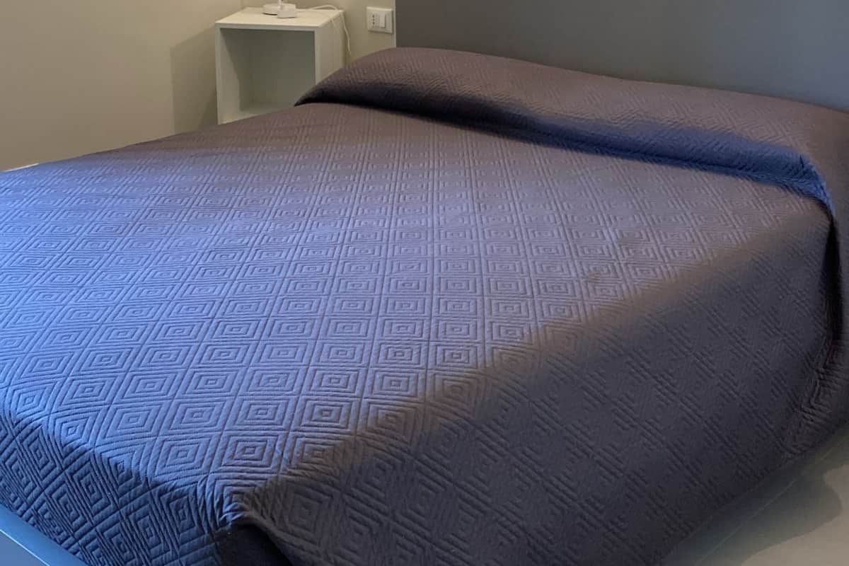 A bedroom with a bed, a nightstand, a wall-mounted lamp, and a framed picture.