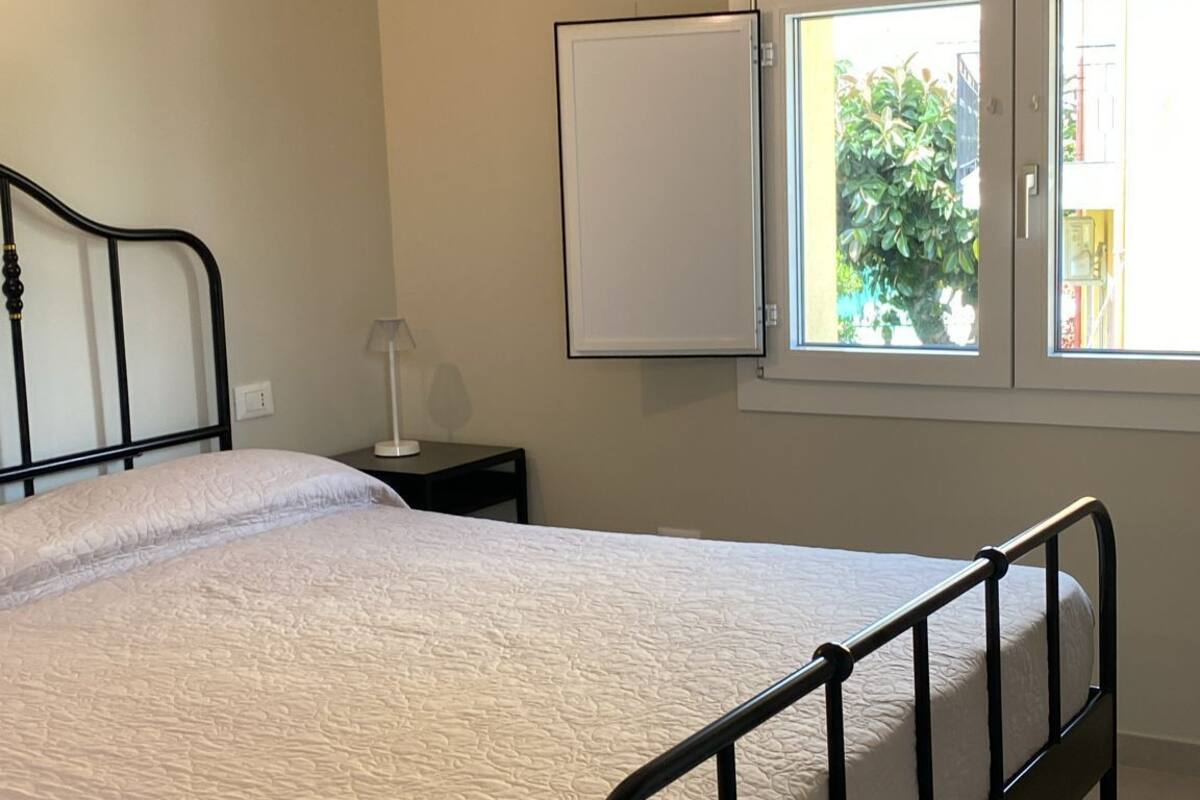 A bedroom with a bed, a nightstand, a window, and a door.