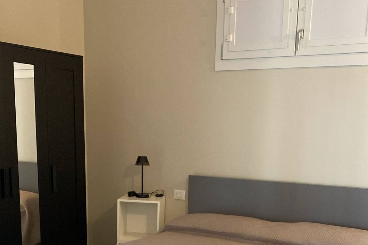 A modern bedroom with a bed, nightstand, and a mirror.