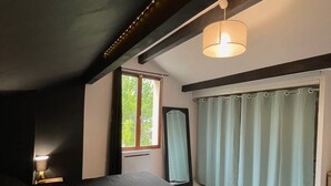 Ett sovrum med en stor säng, ett fönster med gardiner, en hängande lampa och en spegel på väggen.