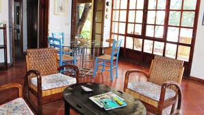 Une pièce meublée de meubles en osier, avec une table en verre et de grandes fenêtres.